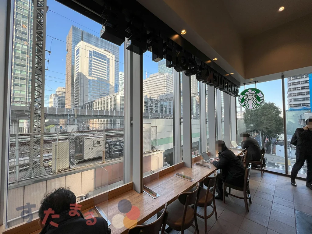スターバックスコーヒー 東京ステーションシティ サピアタワー店の店内のガラス越しに見える東京駅の在来線と新幹線の写真